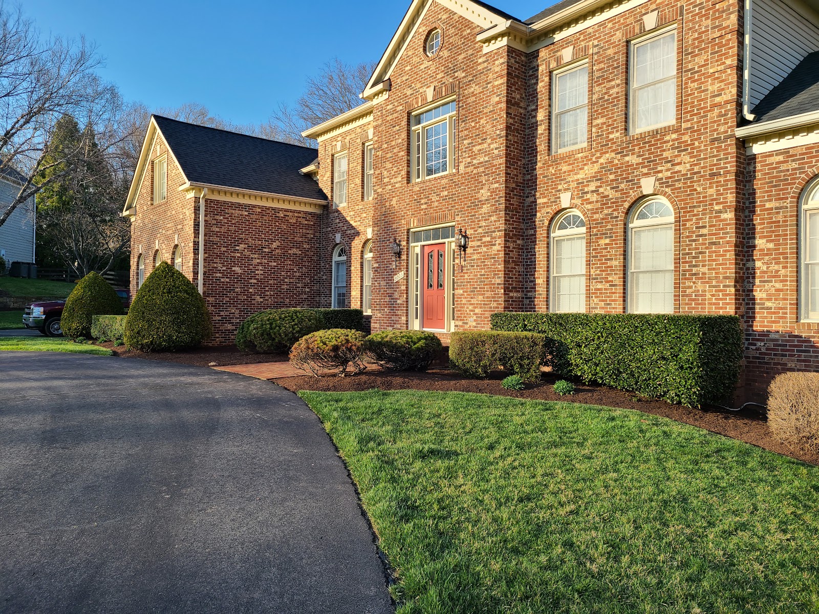 A manicured brick colonial home in Northern Virginia landscaped by APH — trimmed hedges, fresh mulch beds and a crisp green lawn at golden hour